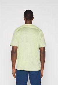 Ανοιχτό πράσινο T-shirt με κοντά μανίκια, διακριτική υφή και στρογγυλή λαιμόκοψη, εμφανιζόμενο από την πίσω πλευρά, συνδυασμένο με σκούρο μπλε παντελόνι.