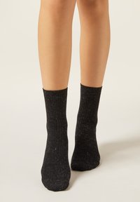 Schwarze Stricksocken mit einer gerippten Textur, mittlerer Wadenlänge und einem dezenten Glitzereffekt. Flache Zehnähte und elastischer Bund für einen guten Sitz.