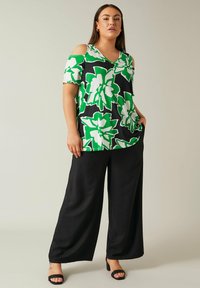 Top nero con scollatura a V e maniche corte, caratterizzato da un grande motivo floreale verde e bianco. Abbinato a pantaloni neri larghi e sandali neri con tacco.