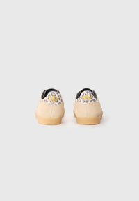 Baskets en suédine beige avec un design de talon en imprimé léopard coloré, doté d'une semelle en caoutchouc texturé et d'un petit logo jaune à l'arrière.