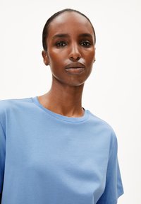 T-shirt en coton bleu clair à manches courtes et col rond, avec une texture douce et un design simple et minimaliste.