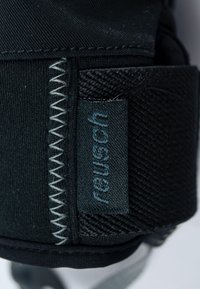 Schwarze Sporthandschuhe aus strukturiertem Stoff, mit auffälliger Naht und einem eingenähten Etikett mit der Aufschrift "reusch." Das Design betont Grip und Langlebigkeit.