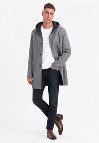 Abrigo de mezcla de lana gris con gran capucha, forro negro, cierres de botón y bolsillos laterales, combinado con jeans de mezclilla oscura y botas de tobillo marrones.