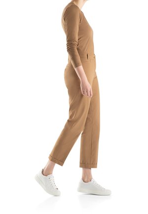 Haut à manches longues marron associé à un pantalon marron clair. Le mannequin porte des baskets blanches. Tissu lisse, design ajusté et poignets roulés sur le pantalon.