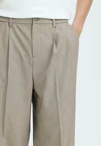 Beige, gestructureerde broek met een getailleerde pasvorm. Heeft een enkele plooien, zijzakken en een knoopsluiting in de taille.