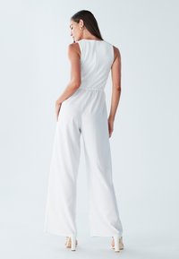 Witte overall met een nauwsluitend lijfje en wijde broekspijpen. Geweven rugpaneel, elastische taille en stijlvolle hakken zijn zichtbaar.