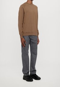 Bruine sweatshirt met lange mouwen, voorzien van een geribde hals en manchetten, gecombineerd met grijze rechtvallende jeans en zwarte sneakers. Minimalistisch ontwerp.