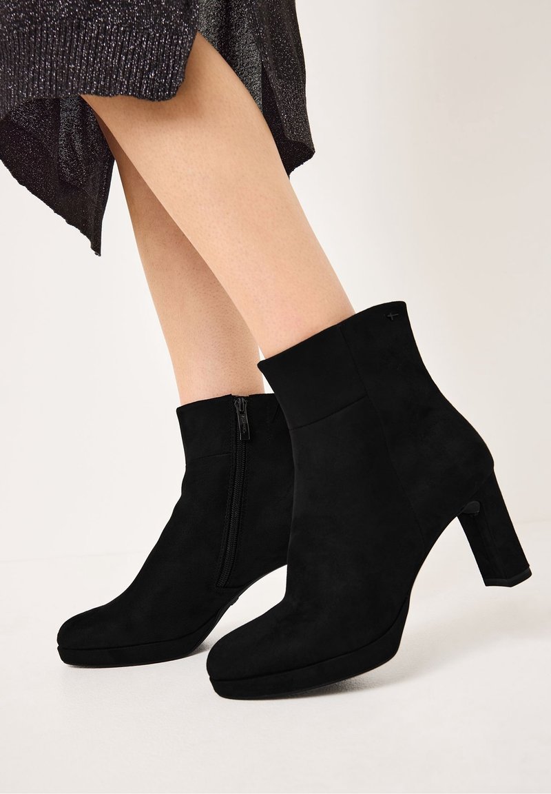 Bottines en daim noir avec talon épais, bout arrondi et fermeture éclair latérale. Texture lisse avec des accents minimalistes, conçues pour une silhouette élégante.