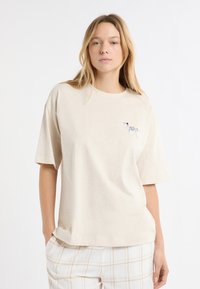 Jasnobeżowa koszulka wykonana z miękkiego materiału, z krótkim rękawem i małą haftowaną psinką na lewej piersi.