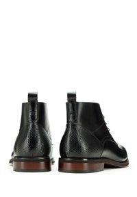 Botas de tobillo negras de cuero con parte trasera texturizada, diseño con cordones, punta redondeada y suela de madera en contraste. Incluyen lengüetas para facilitar su puesta.