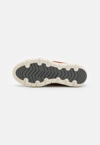 La suela del zapato SOREL presenta un patrón de goma gris con acentos elevados, rodeado de un borde de amortiguación blanca. Superficie texturizada para un mejor agarre.