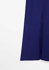 Den nedre halvan av en mörkblå kjol med en slits bak i mitten, visad mot en vit bakgrund.