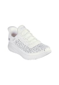 Zapatilla deportiva blanca con parte superior texturizada con pequeños puntos negros, cordones elásticos y suela blanca acolchada.