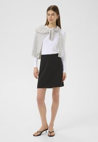 Jupe noire, haut à manches longues blanc, et pull gris drapé sur les épaules. Coupe slim, texture lisse, style décontracté, design minimaliste.