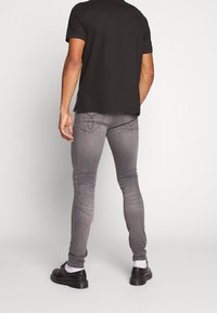 Jeans skinny grises con textura desgastada y costuras en contraste, combinados con una camiseta negra y zapatos negros, vistos desde atrás.