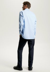 Camicia azzurra a maniche lunghe con orlo curvo e polsini a bottone, abbinata a pantaloni blu navy e scarpe nere. Tessuto morbido e vestibilità rilassata.
