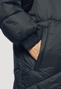 Giacca a vento nera con texture trapuntata, dotata di una tasca laterale e polsini elasticizzati per una vestibilità aderente. Materiale morbido e leggero.