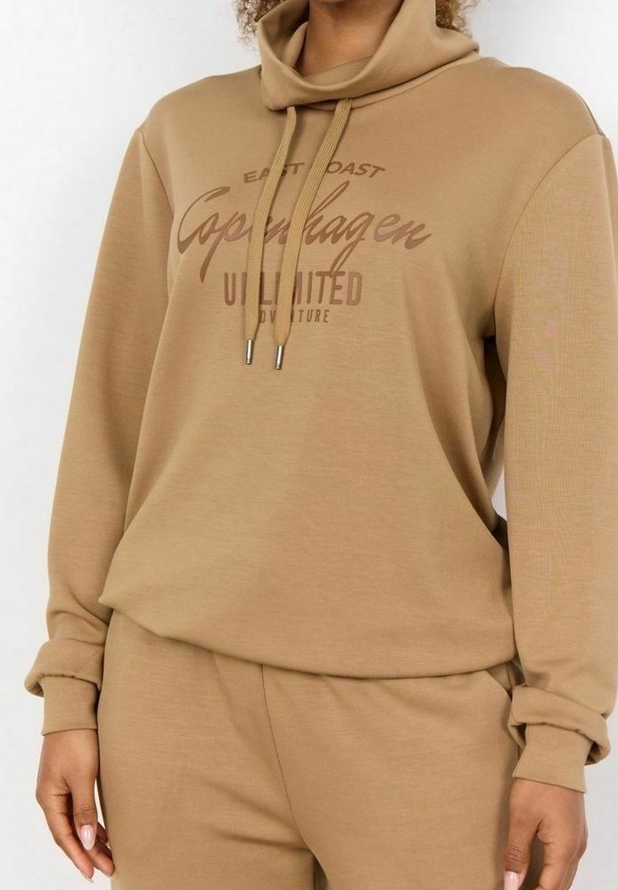 Sweat à capuche beige avec texte devant "East Coast Copenhagen Unlimited Adventure", doté d'un col boule et de cordons de serrage, accompagné d'un pantalon assorti.