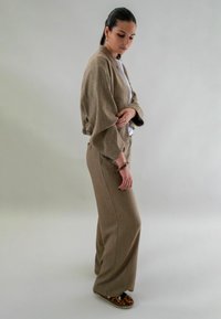 Lichtbruine cropped jas en bijpassende hoge taille broeken, beide in een gestructureerde stof. Het model draagt een witte top en schoenen met luipaardprint.