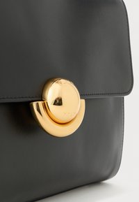 Fekete bőr táska lekerekített arany csattal, amelyen a "Furla" márkaneve található az elülső fedélen.