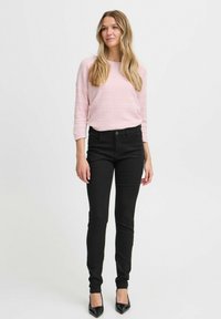 Zwarte skinny jeans gecombineerd met een lichtroze gestructureerde trui, met driekwartmouwen en een losse pasvorm. Zwarte hoge hakken.
