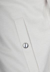 Tessuto bianco con un'apertura rettangolare cucita che presenta un bottone argento inciso con il testo "GLAVENTA MILANO."