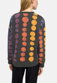 Ciemnoszara bluza z okrągłymi, kolorowymi wzorami w odcieniach pomarańczowym, żółtym, fioletowym i niebieskim; ściągacze na mankietach i dekolcie.
