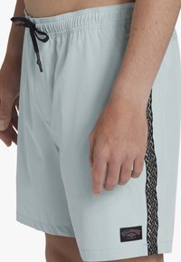 Shorts de bain bleu clair avec une taille élastique dotée d'un cordon noir, décorés d'une bande latérale noire à motifs et d'un patch logo.