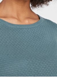 Světlomodrý svetřík s kulatým výstřihem a texturovaným pleteným vzorem. Látka má jemný vzor malých vystouplých teček.