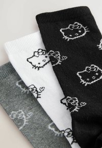 Drie paar katoenen sokken in grijs, wit en zwart; elke sok heeft een herhaald Hello Kitty-patroon in contrasterende kleuren.