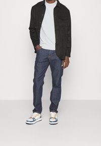 Czarna koszula z guzikami, jasnoszara sweter, ciemnoniebieskie dżinsy i wielokolorowe sneakersy z niebieskimi akcentami. Swobodny, warstwowy strój.