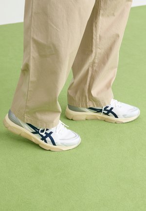 White and navy athletic sneakers with mesh and synthetic material, featuring a thick sole and textured accents. Paired with beige pants.