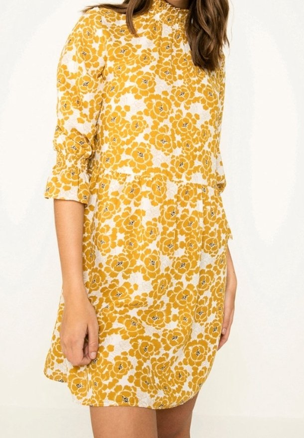 Vestido floral amarillo con fondo blanco, de mangas largas y puños fruncidos. La tela tiene un aspecto texturizado y un corte holgado.