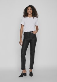 Pantalones de cuero negro de talle alto con ajuste slim, combinados con una camiseta blanca de algodón sencilla y mules negros de tacón. Textura suave.