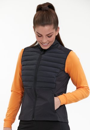Zwarte puffer vest met horizontale stiksels, geribbelde kraag en zijzakken, gecombineerd met een oranje langemouwen basislaag.