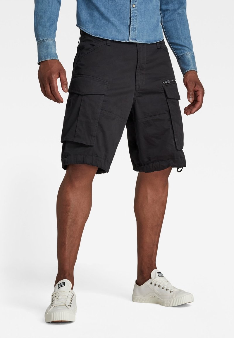 Svarta cargoshorts i lätt tyg, med flera fickor, justerbara benslut och en avslappnad passform, i kombination med vita sneakers.