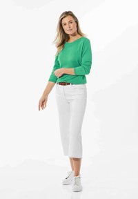Groene, lange mouw sweater gecombineerd met witte cropped broek en witte sneakers. Heeft een ronde halslijn en een riem in de taille.