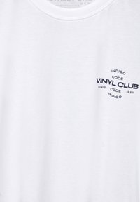 Vit bomulls T-shirt med rund halsringning och en svarttryckt logotyp som inkluderar texten "VINYL CLUB" och "INDIGO CODE."