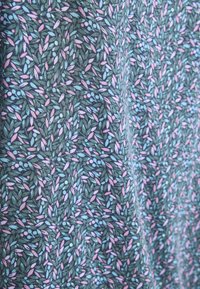 Mönstrad tyg med en grön bakgrund och små rosa och blå bladliknande former i en blommig design. Slät textur, bomullsmaterial.