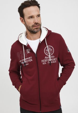 Bordo dukserica na zip s kapuljačom obrubljenom bijelim, koja sadrži otisnuti tekst i grafiku, prednje džepove, te rebraste manžete i donji rub.