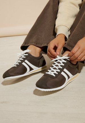 Bruine sportschoenen met witte race-strepen, vetersluiting, faux leer, rubberen zolen en contrasterende textuuraccenten op de neus.