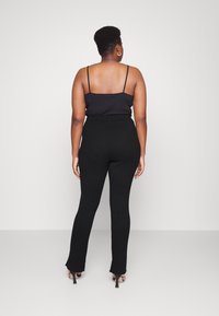 Leggings pretos canelados com uma cintura alta, combinados com um camisola justa preta, vistos de costas. Saltos agulha completam o visual.