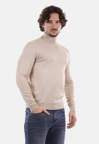 Maglione beige a collo alto realizzato in un morbido e liscio tessuto a maglia. Presenta maniche lunghe e un design aderente con polsini e orlo a coste.