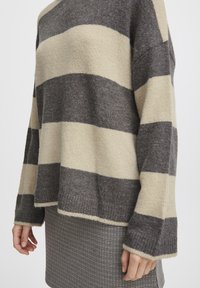 Pull rayé avec des bandes alternées de gris foncé et beige, fabriqué en mélange de laine douce, avec une coupe décontractée et des poignets côtelés.