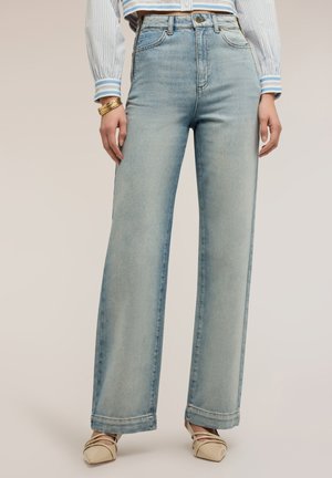 Světlé modré džíny s vysokým pasem a širokými nohavicemi, nošené s proužkovanou blůzou s dlouhým rukávem, zlatými náramky a béžovými lodičkami s špičatou špičkou.