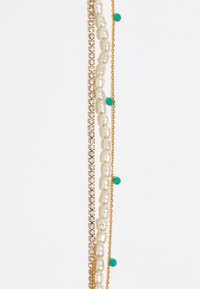 Joyería en tono dorado que presenta una mezcla de perlas, cuentas verdes y pedrería, dispuestas en hebras en capas con texturas variadas.