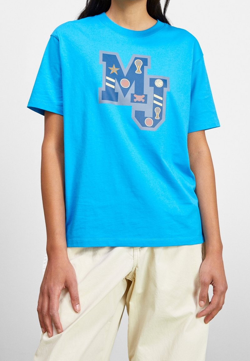 Camiseta de algodón azul brillante con mangas cortas que presenta un gran gráfico "MJ" en gris y acentos coloridos como estrellas y círculos.