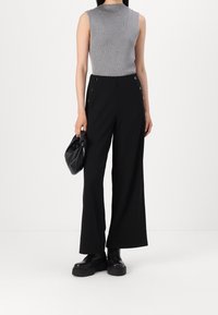 Grijs mouwloos topje met een geribbelde textuur, gecombineerd met hoge zwarte wijde broek met knoopaccenten en een gladde afwerking.