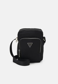 Črn najlonov crossbody nahrbtnik z zlatim zadrgo, poudarkom na logotipu in nastavljivim trakom. Gladka tekstura in kompakten pravokoten oblik.