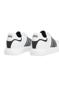 Bijele tenisice s crnim prugama i naglascima, koje imaju gumeni potplat, zaobljen nos i utisnut detalj "1973" na peti.